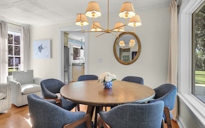 A dining area with a round table, blue chairs, a chandelier, a mirror, and a painting on the wall.