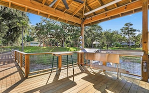 A wooden deck with a railing, overlooking a body of water and a grassy area with trees.