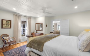 A bedroom with a bed, a dresser, a chair, a window with curtains, and a ceiling fan.