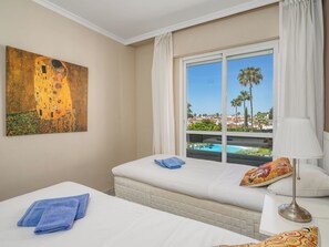 Habitación de hotel con cama, ventana con vista a una piscina y palmeras, y un cuadro en la pared.