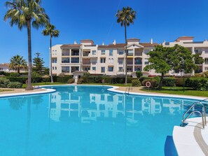 Una piscina con agua azul cristalina, rodeada de palmeras y un edificio de varios pisos con balcones.