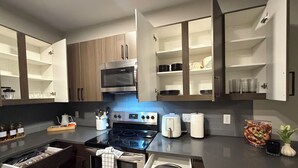 Una cocina moderna con electrodomésticos integrados, armarios abiertos y una encimera con diversos objetos.