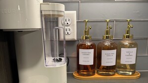 Una cafetera, una jarra de vidrio y tres botellas de sirope de café sobre una encimera.