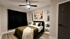 Un dormitorio con cama, ventilador de techo, mesita de noche, espejo y puerta.