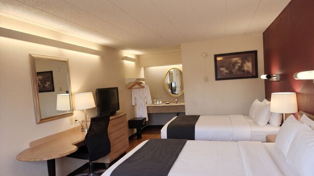 Une chambre d’hôtel avec deux lits, un bureau, une chaise, une télévision, un miroir, un peignoir et une salle de bain équipée d’un lavabo et d’un miroir.