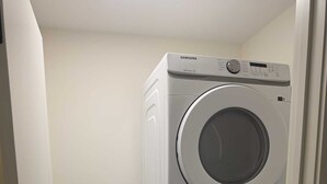 Un lavadero con dos lavadoras Samsung apiladas, una puerta y un suelo con baldosas hexagonales.