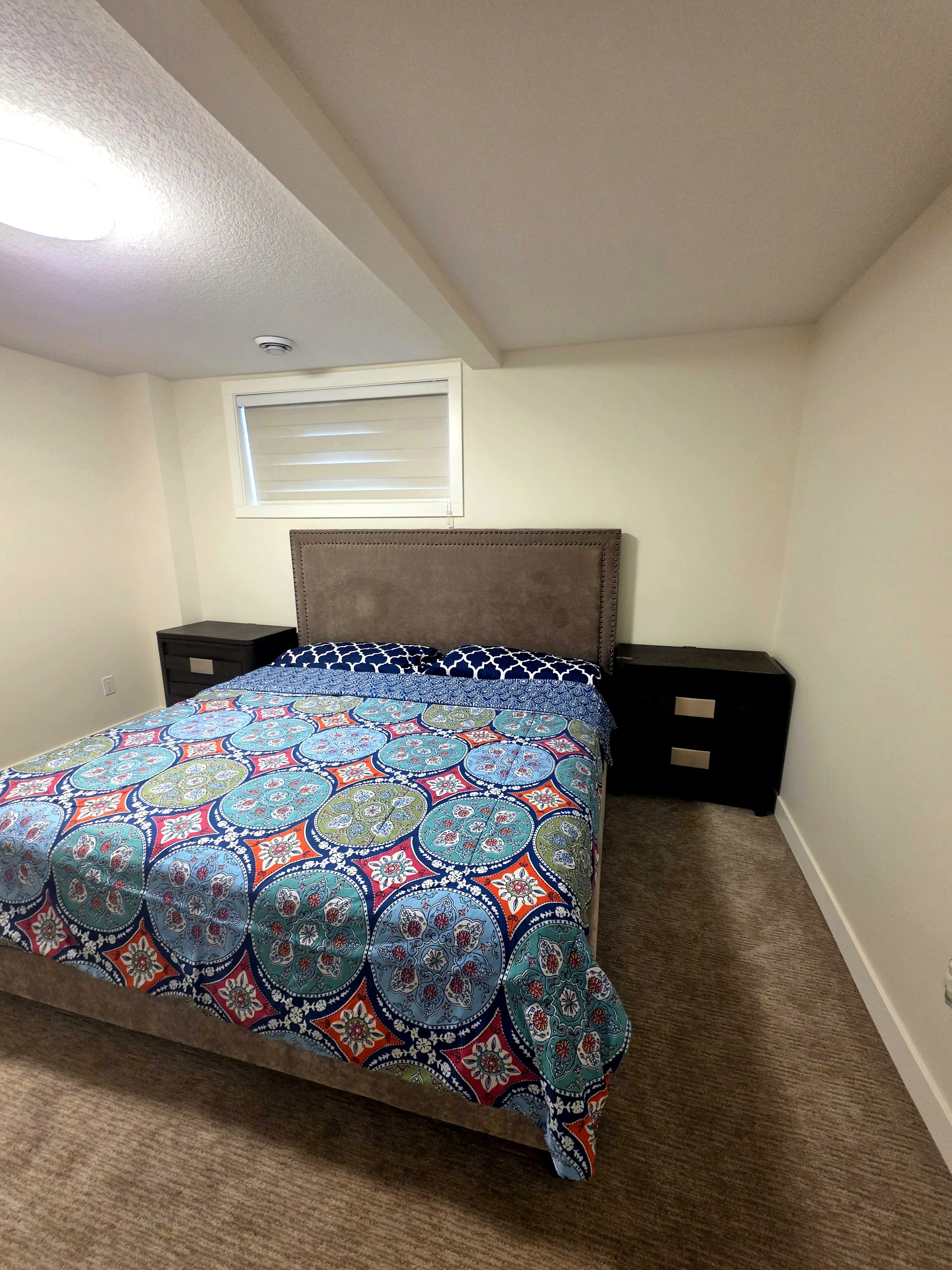 Un dormitorio con cama, cabecera, mesitas de noche y una ventana.