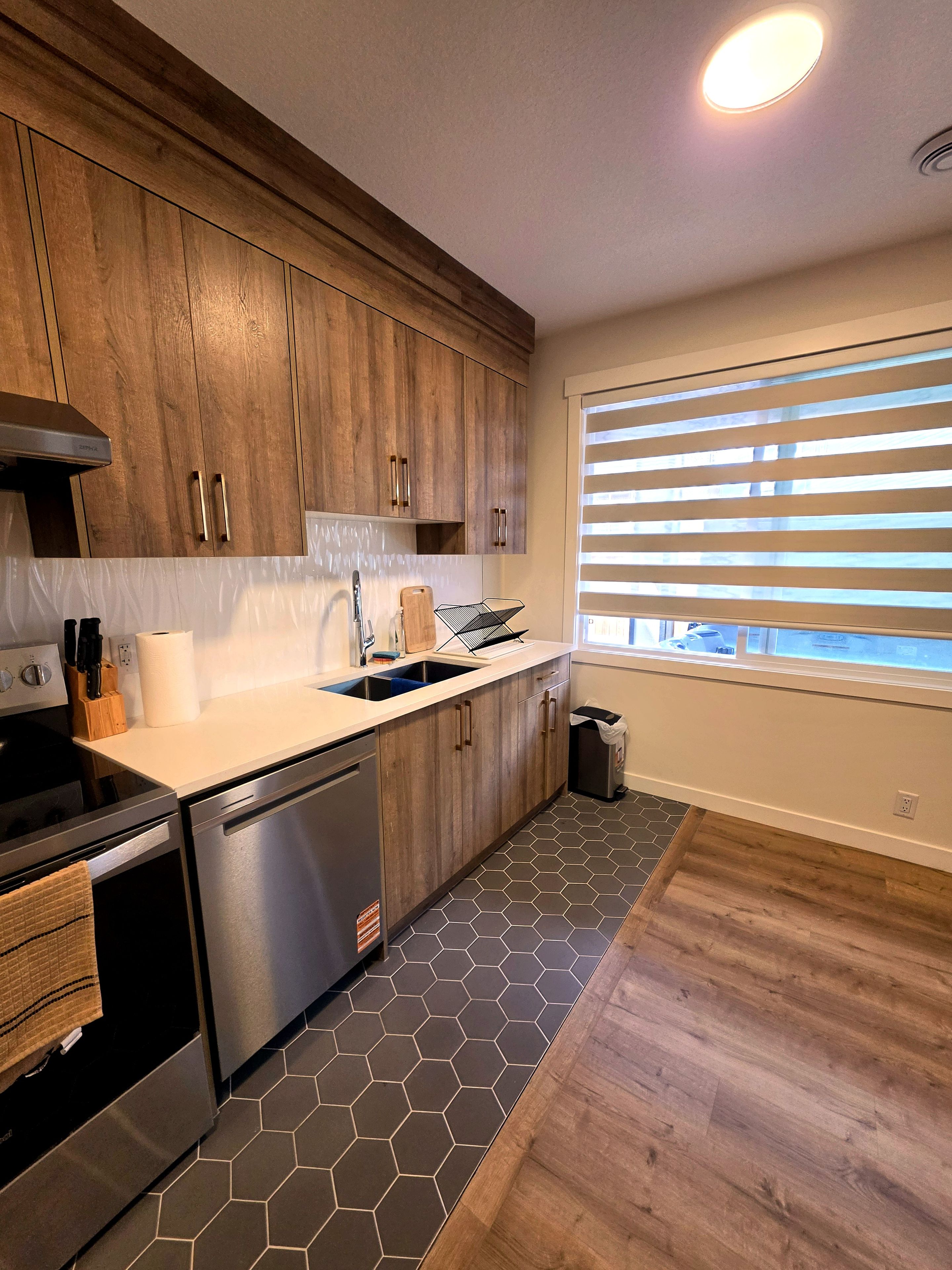 Une cuisine moderne avec des meubles en bois, des appareils électroménagers en acier inoxydable et un sol carrelé à motifs hexagonaux.