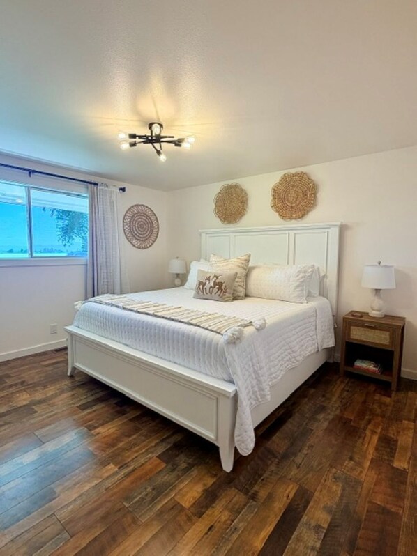 A bedroom with a large bed, wooden flooring, a ceiling light fixture, and decorative wall art.