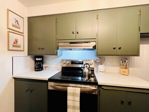 A kitchen with green cabinets, a stove, a kettle, and a coffee maker.