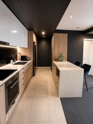 A modern kitchen with a central island, built-in appliances, and a dark accent wall. - Luxury CBD Apartment | Pool & Gym | Walk to Queen St | Views (Brisbane City)