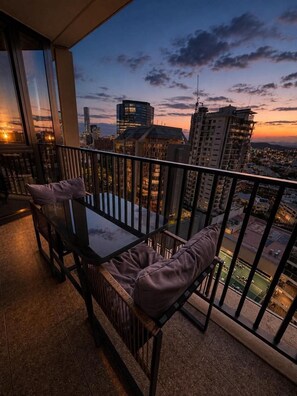 A balcony with a table and chairs, offering a city view at dusk. - Luxury CBD Apartment | Pool & Gym | Walk to Queen St | Views (Brisbane City)
