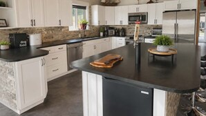 Une cuisine moderne avec des meubles blancs, un îlot central, des appareils en acier inoxydable et un plafond en bois.