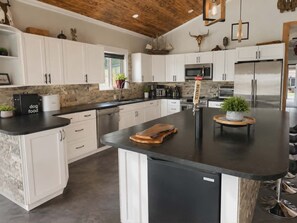 A modern kitchen with white cabinets, a central island, stainless steel appliances, and a wooden ceiling. - Okanagan Hideaway, Lake views & Outdoor Adventure, pet friendly and fun! (Vernon)