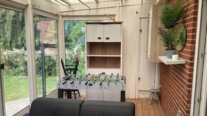 Um espaço interno com mesa de pebolim, um sofá e uma parede de tijolos.