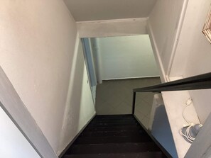 A narrow stairway with a black handrail and a light switch on the wall.