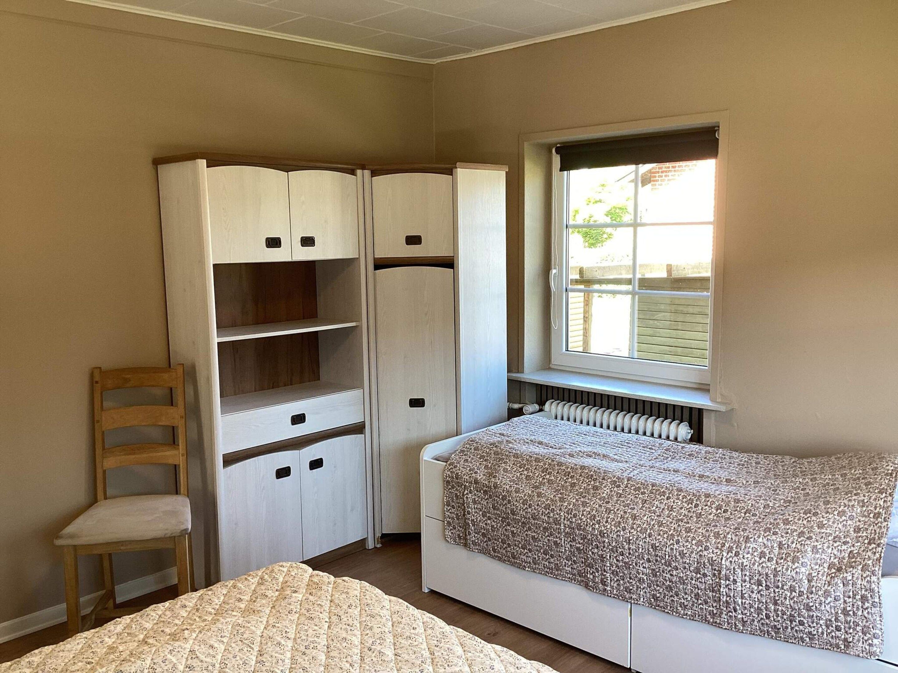 A bedroom with a bed, a wardrobe, a chair, and a window.