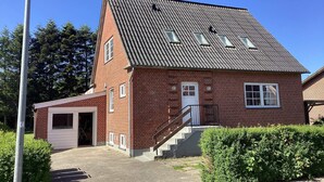 Um edifício de tijolos vermelhos com telhado inclinado, entrada frontal, escadaria e uma pequena garagem anexa.