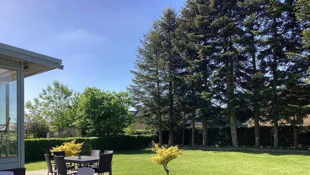 Uma área de pátio com mesa e cadeiras, cercada por um gramado bem cuidado e árvores altas.