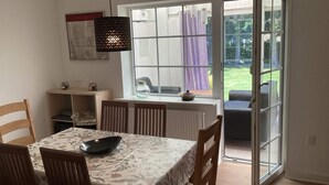 Uma área de refeições com mesa, cadeiras, luminária pendente e vista para o exterior através de uma porta de vidro.