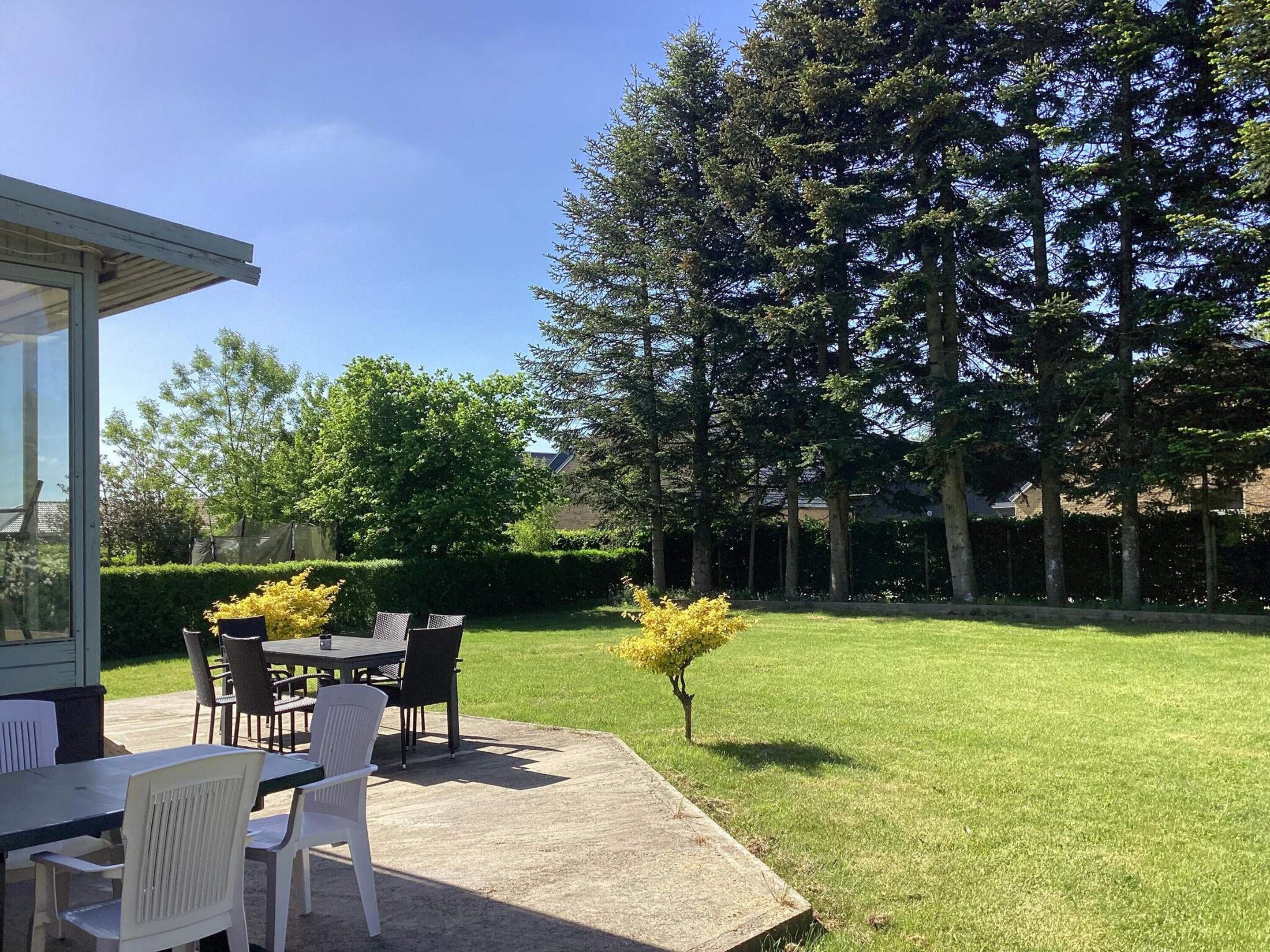 An outdoor patio area with a table and chairs, surrounded by a well-maintained lawn and tall trees.