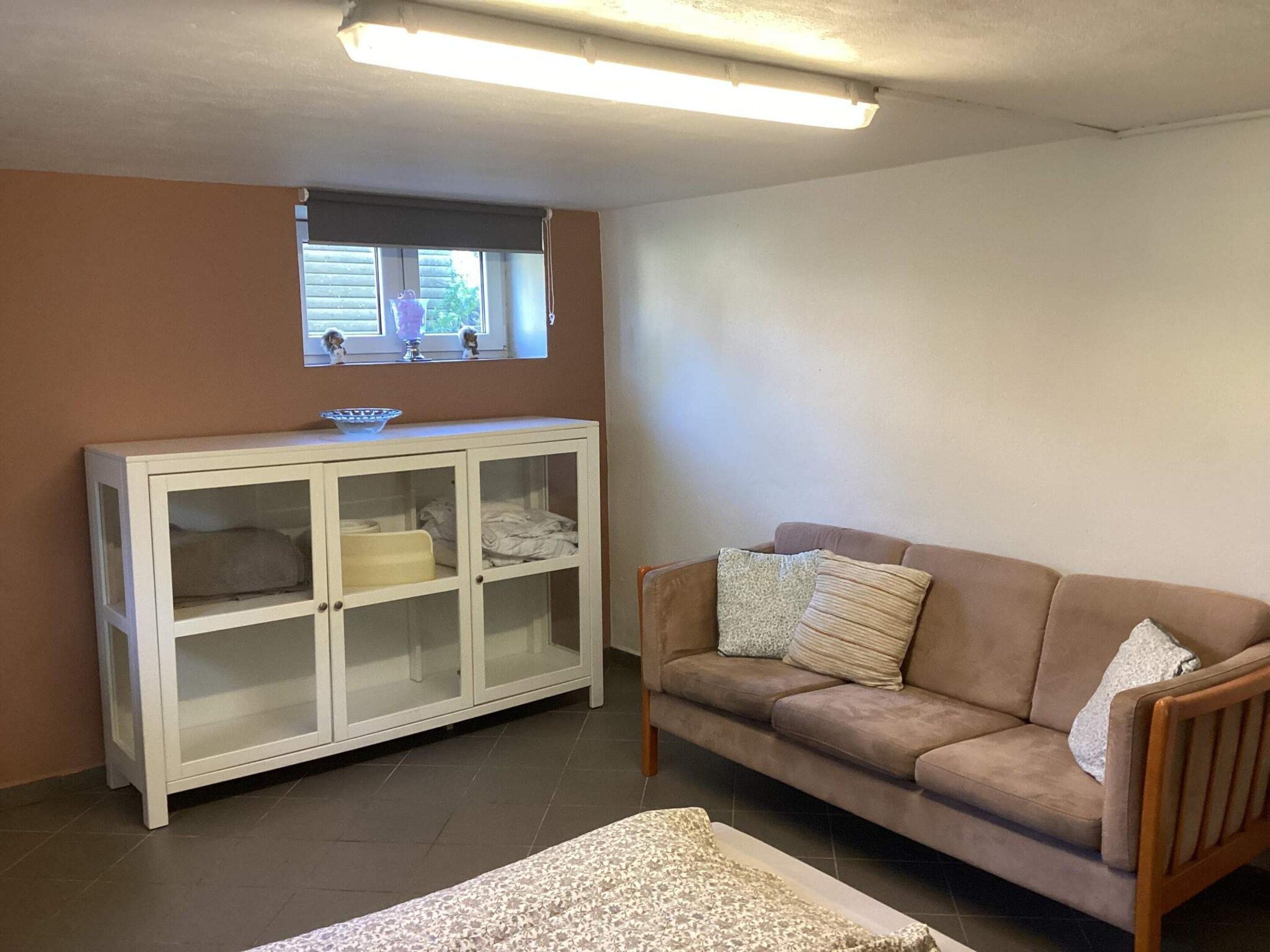 A living room with a beige sofa, a white cabinet, and a window with blinds.