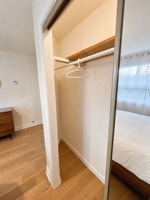 Ein Schlafzimmer mit Holzboden, einem Bett, einem weißen Kleiderschrank und einer Kleiderstange.