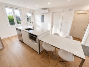 Et moderne køkken med en hvid bordplade, rustfrie stålapparater og et spiseområde med et hvidt bord og stole.