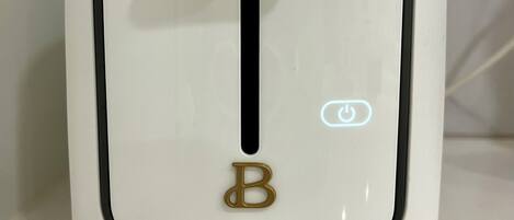 A white appliance with a black control panel, a gold letter 'B' button, and a power indicator light.