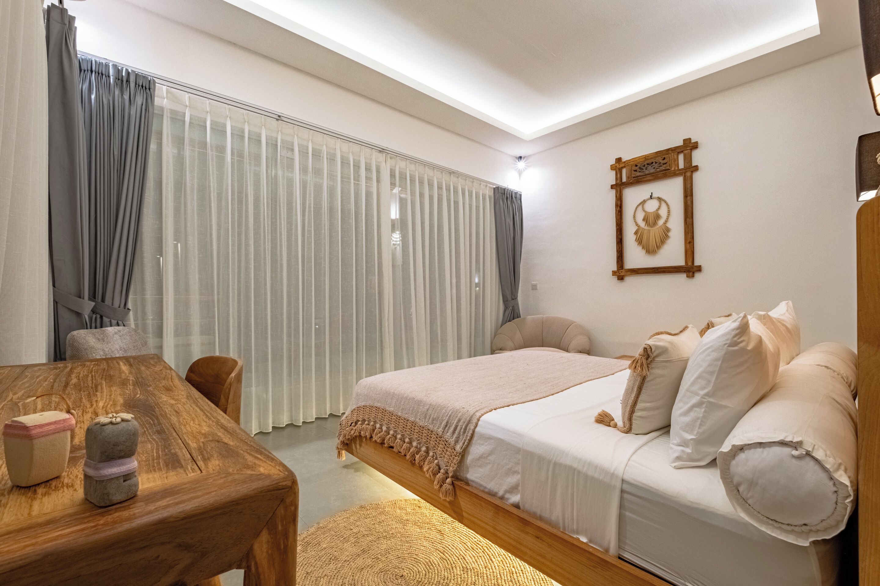 A bedroom with a wooden bed, a bedside table, a chair, a window with curtains, and a wall-mounted decoration.