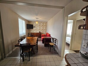 A dining area with a wooden table and chairs, a television mounted on the wall, and a patterned wallpaper. - House for 1–8 people, garden, 10 minutes from Futuroscope and downtown, French decor 1965-1970 (Poitiers)