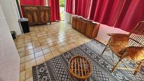 A room with a wooden cabinet, a wicker chair, a patterned rug, and red curtains. - House for 1–8 people, garden, 10 minutes from Futuroscope and downtown, French “ 1965-1970 ” decor (Poitiers)