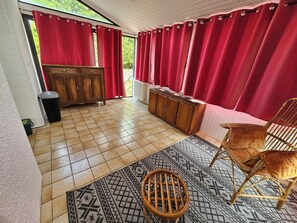 Une pièce avec un meuble en bois, une chaise en osier, un tapis à motifs et des rideaux rouges.