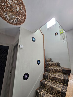 Un escalier recouvert d’une moquette à motifs, un luminaire en fibres tressées et une petite lucarne.