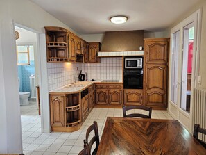 Une cuisine avec des meubles de rangement en bois, un four à micro-ondes, un four traditionnel et une table à manger avec des chaises.