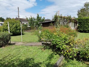 Un patio trasero residencial con un cobertizo de madera, un camino de piedra y diversas plantas y arbustos.