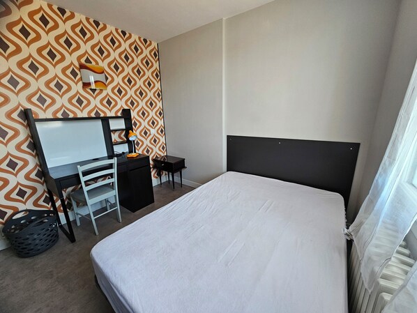 Una habitación de hotel con cama, escritorio, silla y un papel tapiz estampado.