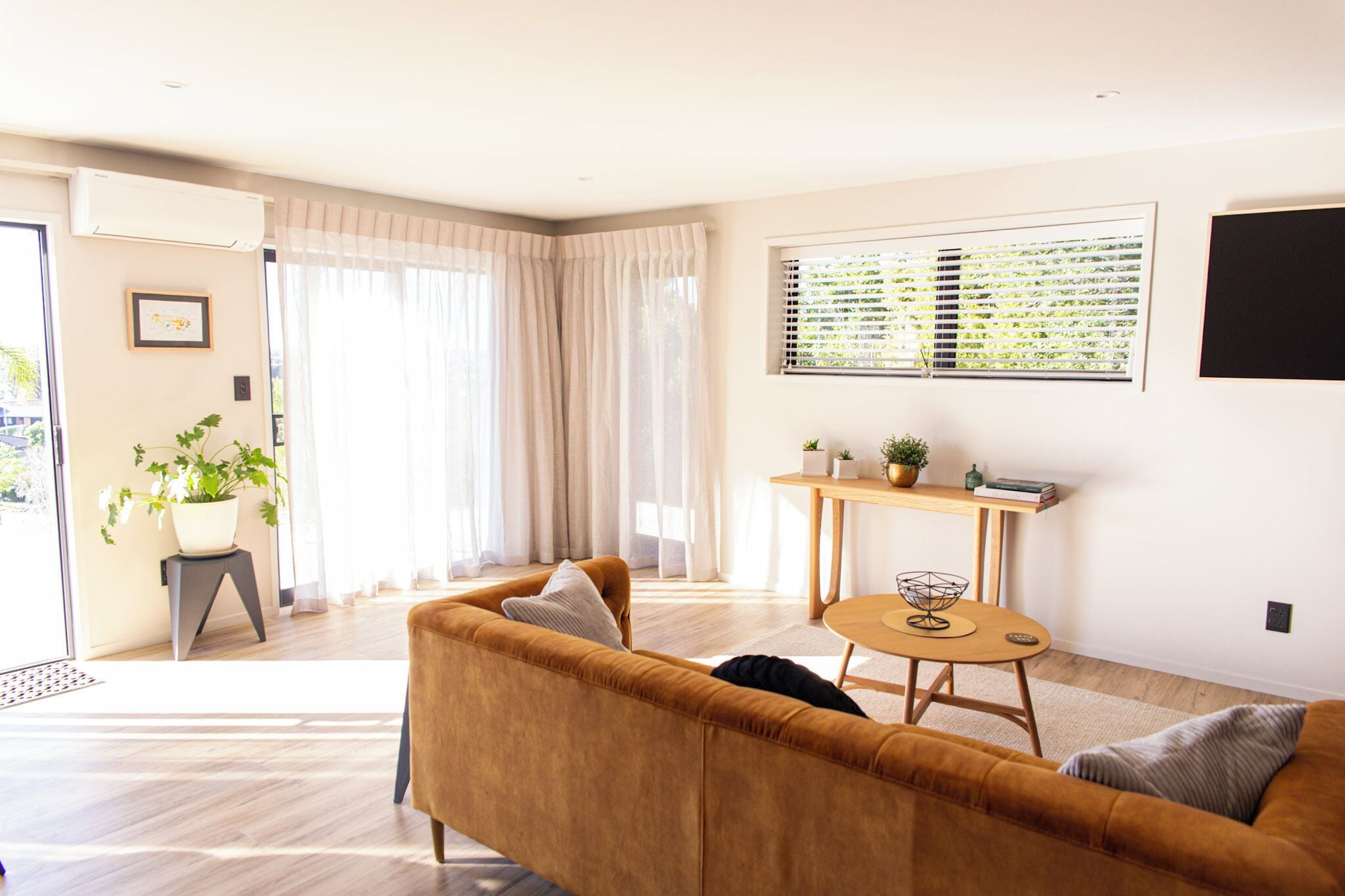 A living room with a sofa, a dining table with a bowl, a potted plant, and a window with blinds.. The Bee Hive