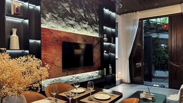 Een moderne eetruimte met een televisie aan een gestructureerde muur, een gedekte eettafel met borden en glazen, en een zithoek met stoelen.