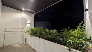 A balcony with a metal drying rack, a white wall, and a row of green plants.
