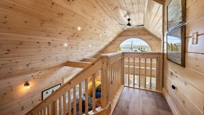 Un intérieur en bois avec un escalier, un ventilateur de plafond et de grandes fenêtres offrant une vue.