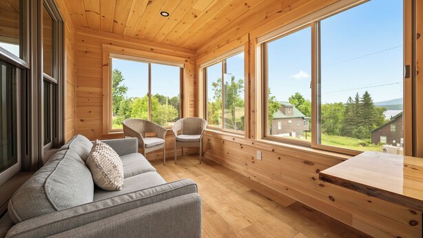 A cabin interior with a sofa, chairs, and large windows offering a view of the outdoors.