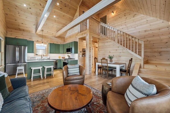 A wooden cabin interior with a kitchen, dining area, and a staircase.