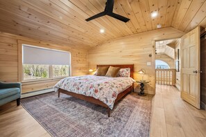 A wooden cabin bedroom with a bed, a nightstand, a lamp, a window, and a door.