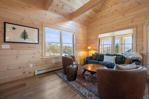 A wooden cabin interior with a large window, a framed picture, a sofa, and a coffee table.