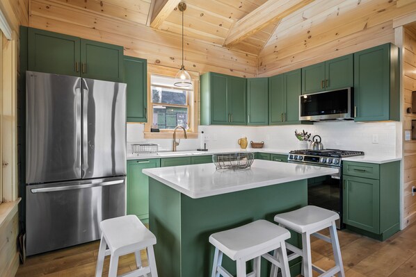 Una cocina moderna con armarios verdes, un refrigerador de acero inoxidable, un microondas y una estufa.