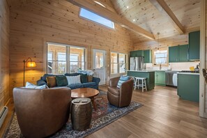 A log cabin interior with a living area, kitchen, and large windows.