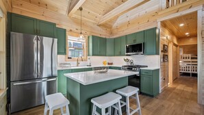 Une cuisine moderne avec des meubles de couleur verte, un réfrigérateur en acier inoxydable, un îlot central doté de tabourets et un four à micro-ondes.