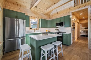 A modern kitchen with green cabinets, a stainless steel refrigerator, a central island with stools, and a microwave.