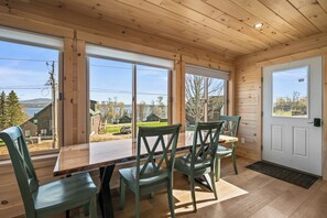 A wooden cabin with a dining area, large windows, and a door.